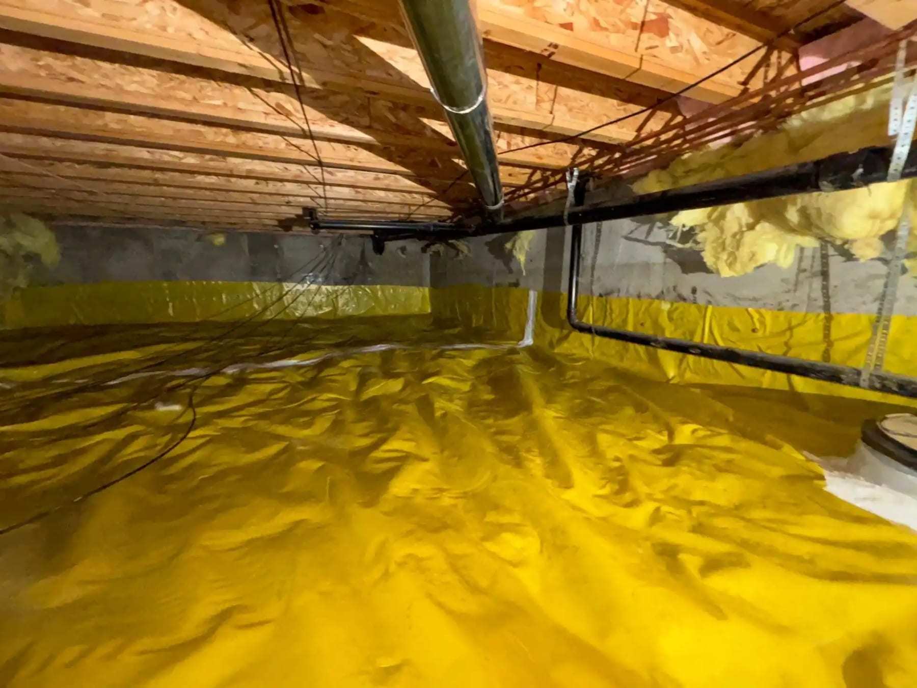 Crawlspace lined with a yellow vapor barrier up the foundation walls