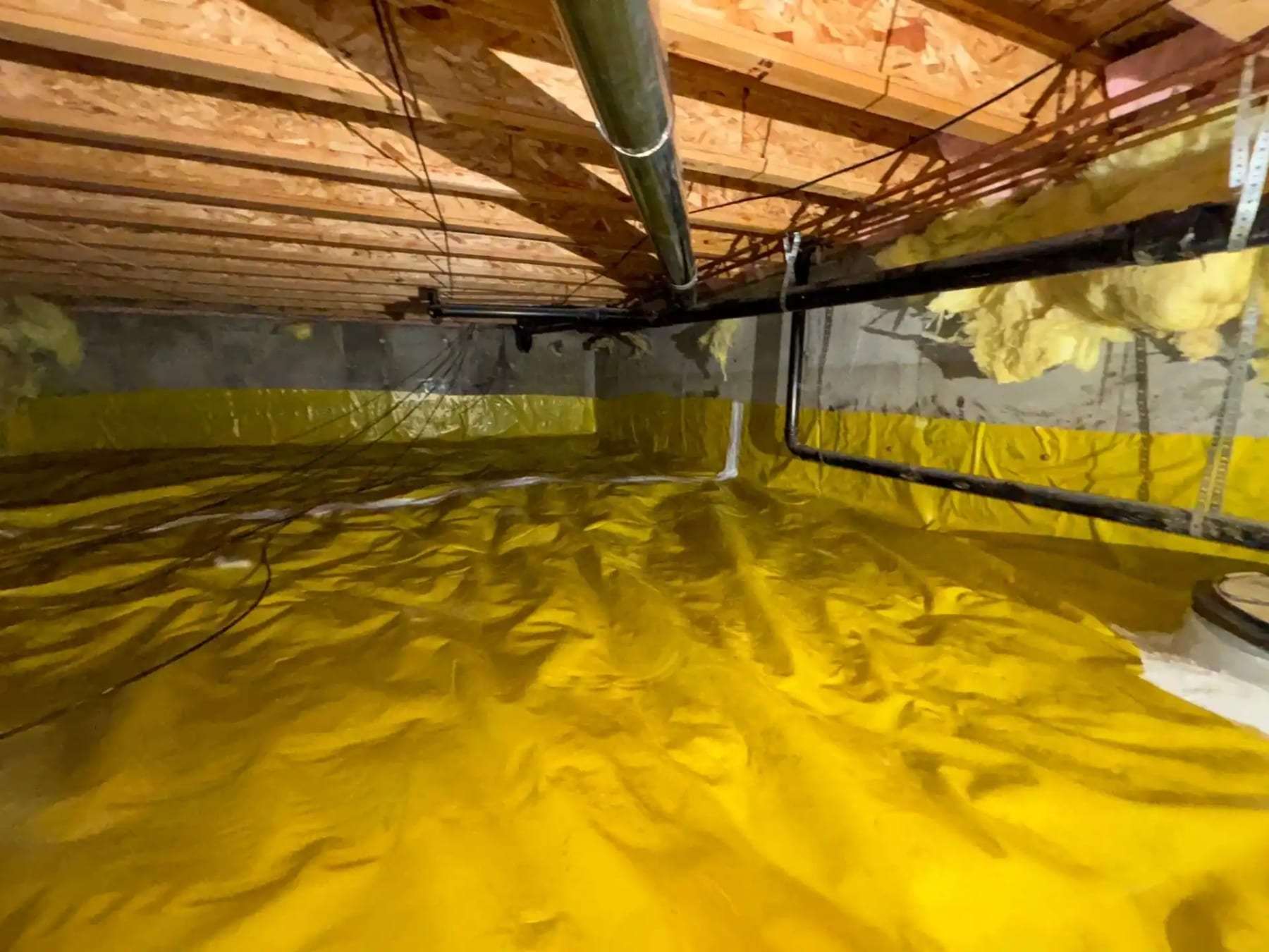 Crawlspace lined with a yellow vapor barrier up the foundation walls