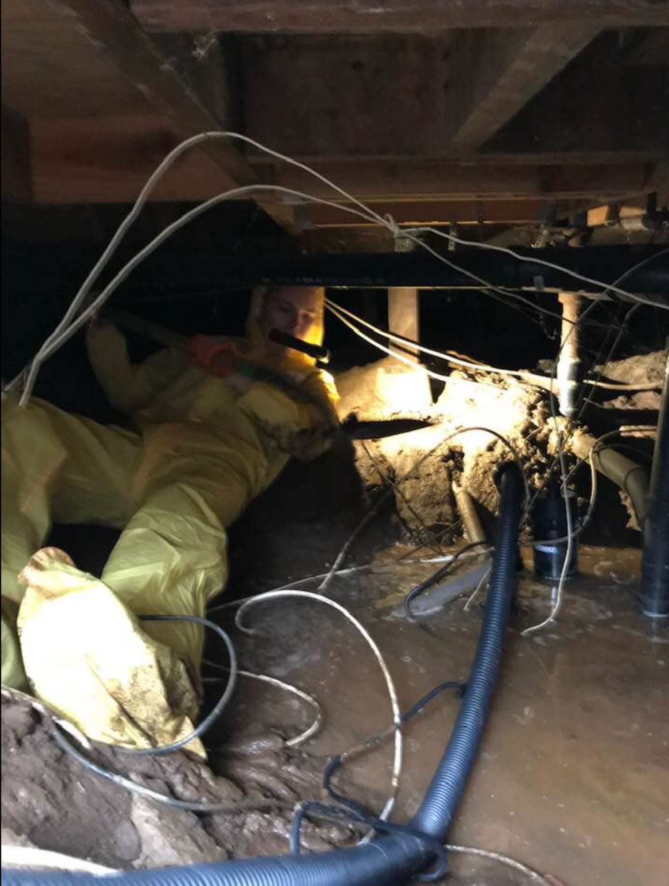 Worker in a yellow protective suit in a muddy crawlspace